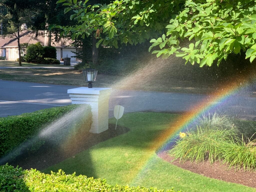 Spring Irrigation Start-Up: A Rainbow of Benefits A rainbow arcs across a lush green lawn being watered by a sprinkler system